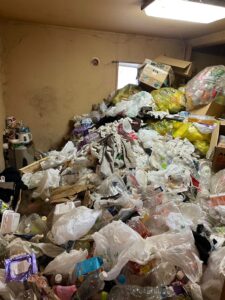 札幌でゴミ屋敷の片付け前の写真。床一面にペットボトルやゴミ袋が散乱し、不用品が山積みの部屋