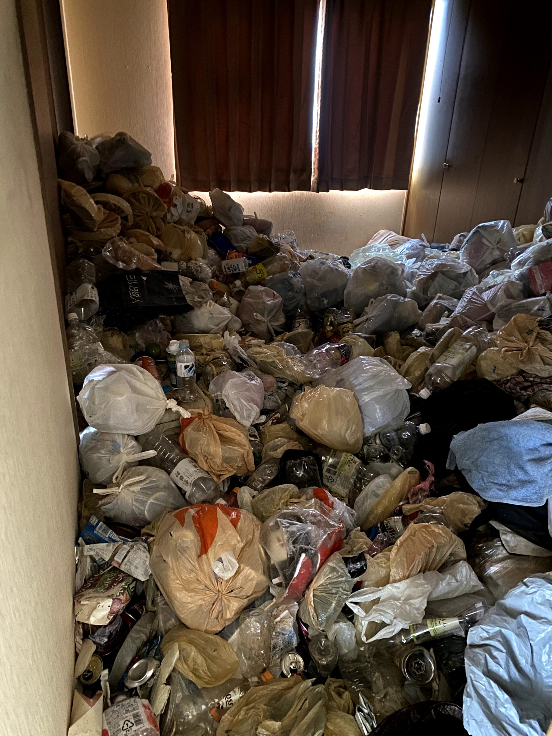 札幌市内のゴミ屋敷片付け前の様子。床一面にゴミ袋やペットボトルが積み重なり、足の踏み場がない部屋のビフォー写真。