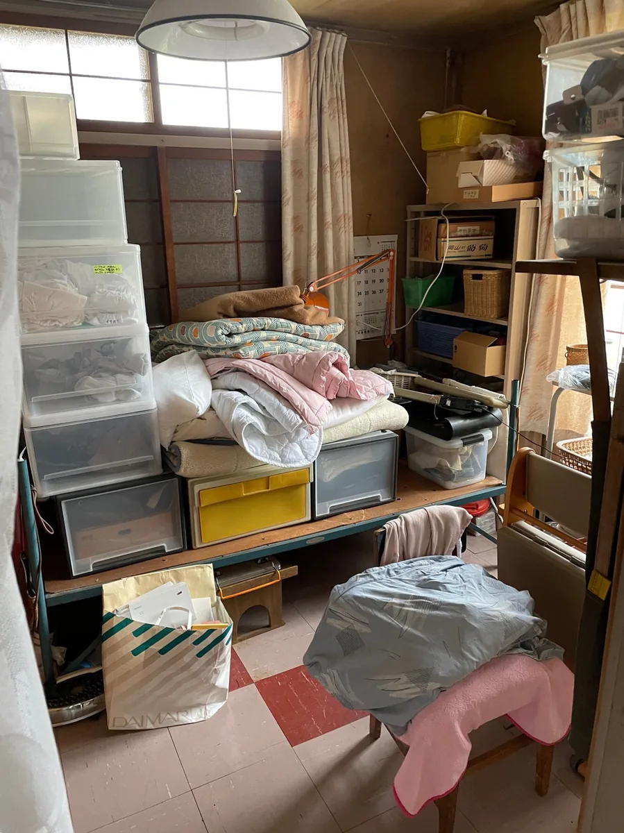 札幌市白石区の遺品整理ビフォー - 洋室に衣装ケースや布団が大量に残された状態